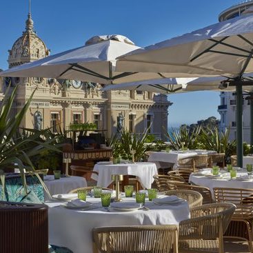 Elegant restaurant terrace in Monaco with parasols, tables and sea views.