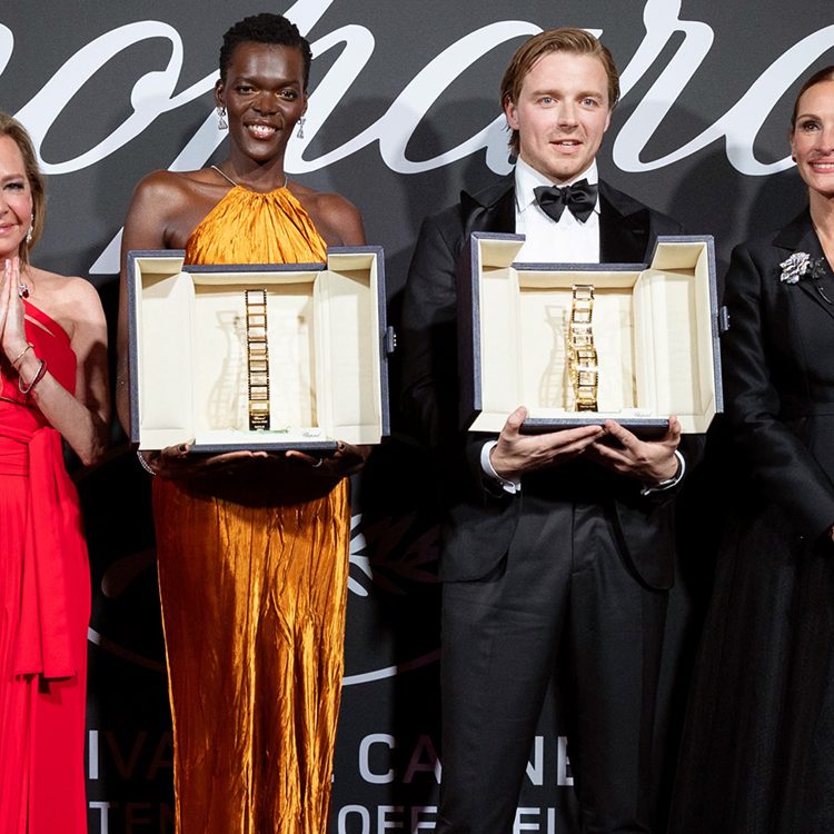 Four smiling people holding trophies on a podium at an event.