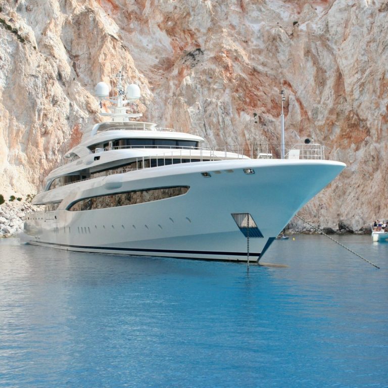 Luxury yacht moored in a cove with cliffs in the background.