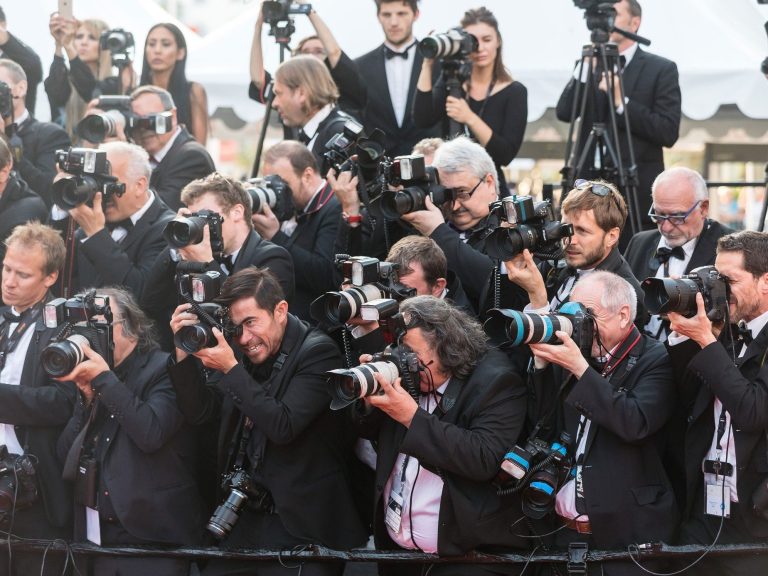 A crowd of photographers in formal wear, capturing moments on a red carpet.