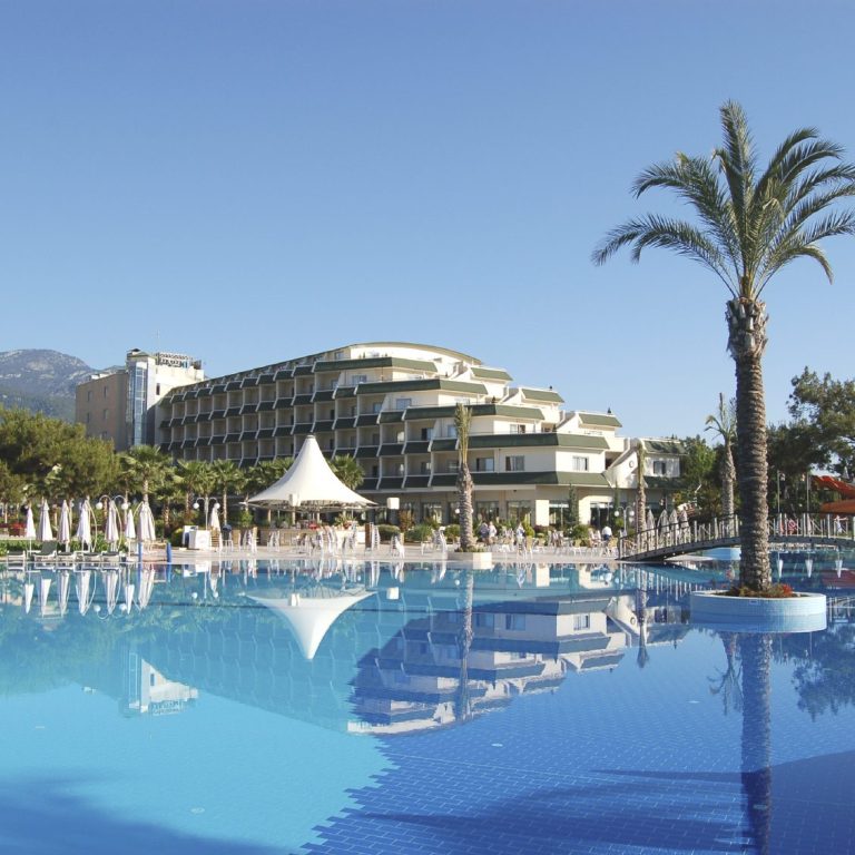 Modern hotel with swimming pool, palm trees and blue sky.