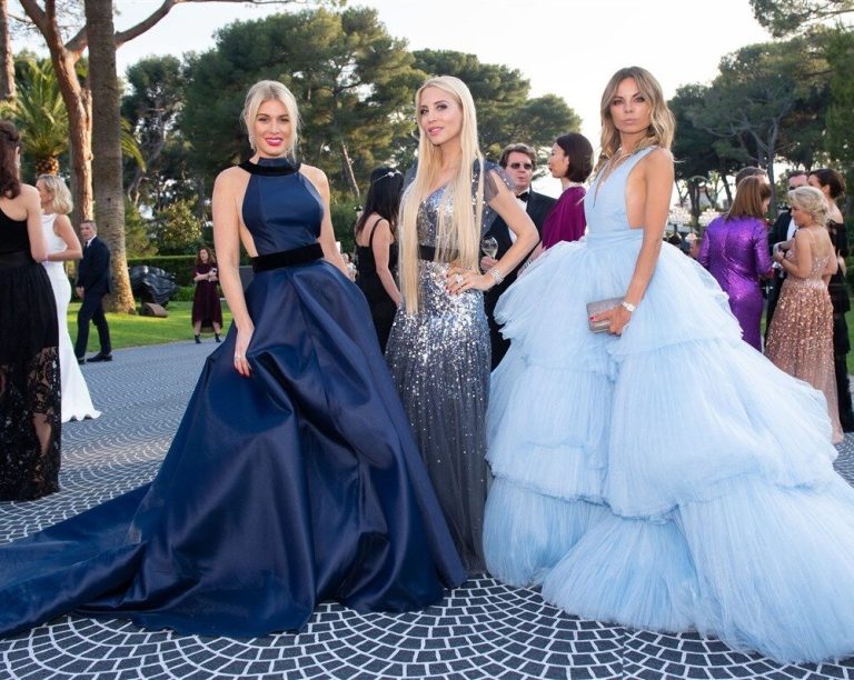 Three elegant women in evening gowns, posing in a chic outdoor setting.