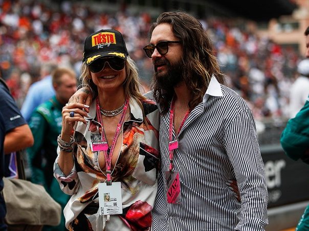 Two smiling people in a crowd, one wearing a cap and the other sunglasses.