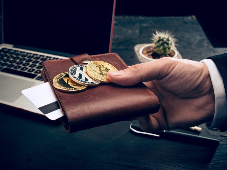 Hand in a wallet with coins and a card, near a computer.