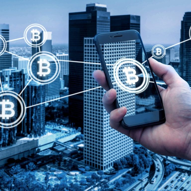 Hand holding a smartphone with Bitcoin symbols on a background of buildings