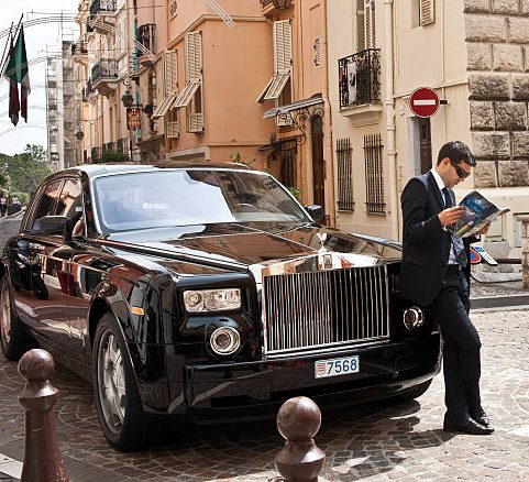 A man in a suit stands beside a black Mercedes sedan.