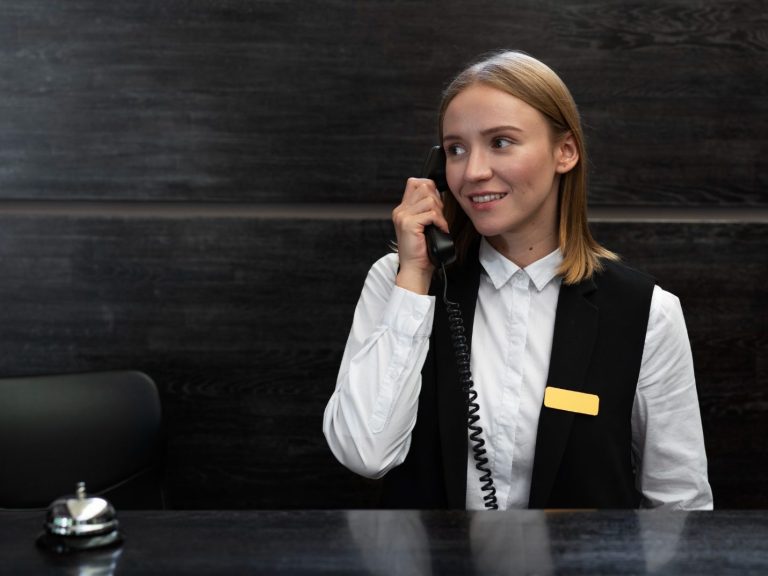 Smiling receptionist on the phone, wearing black vest and white shirt.