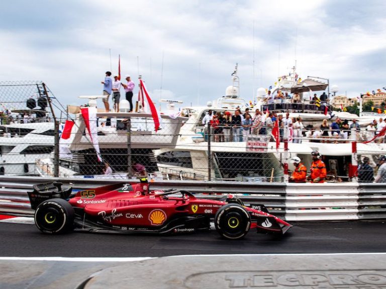 Red Ferrari racing car, passing yachts at the edge of a runway.