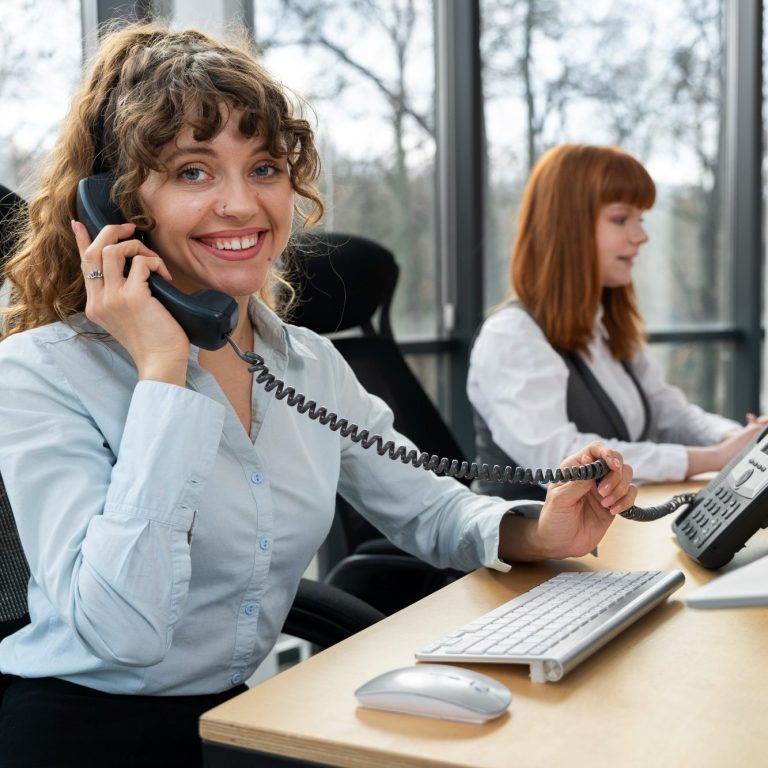 Two women in the office, one talking on the phone and the other using a computer.