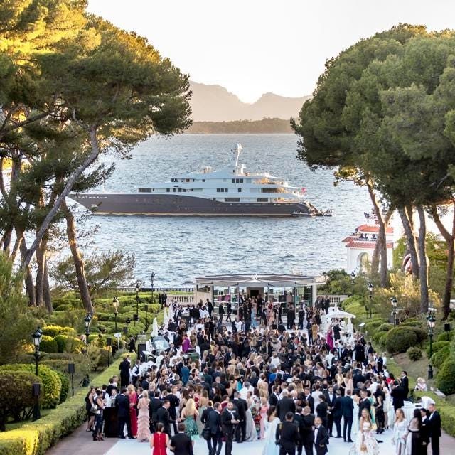 Open-air celebration on the water's edge, with guests and a yacht out to sea.