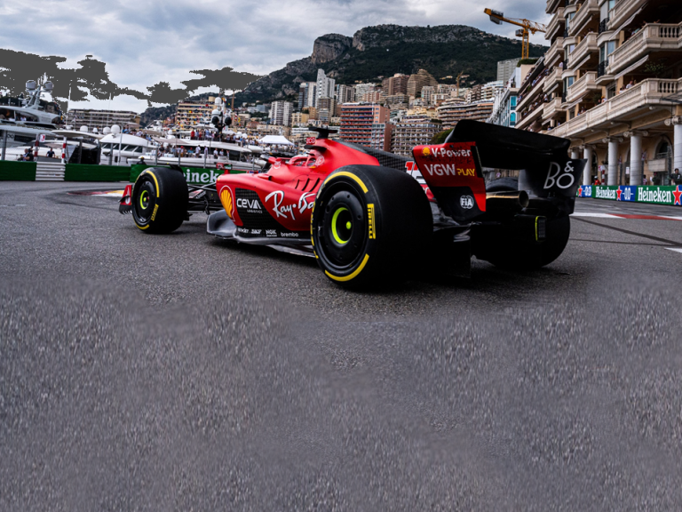 Red Formula 1 car on a bend in Monaco, with yachts in the background.