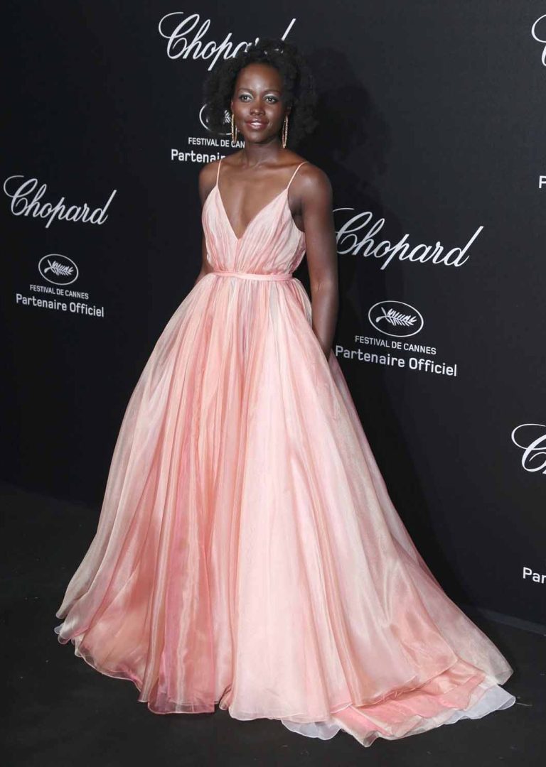 Woman in long pink dress, smiling on black background with Chopard logo.