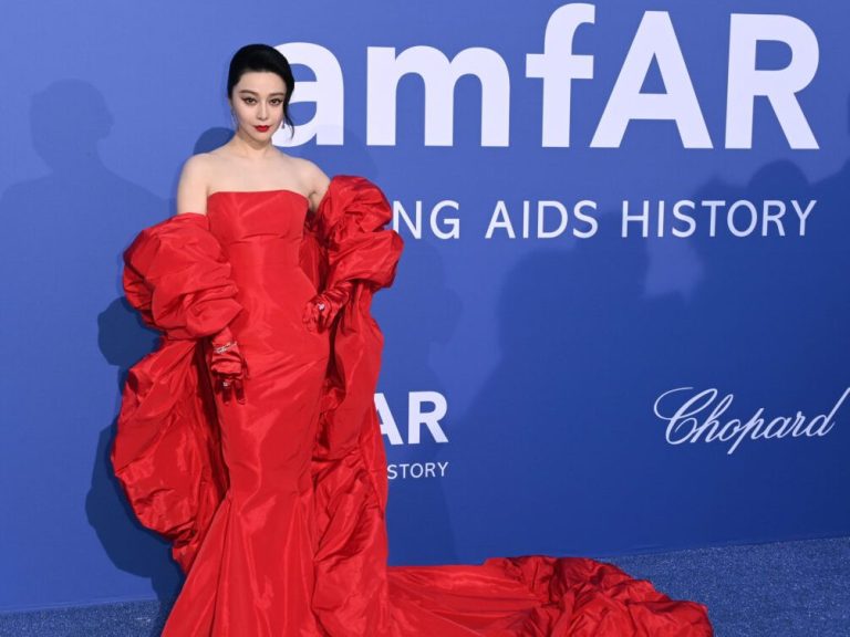 Woman in loose red dress with ruffles, posing on a red carpet.