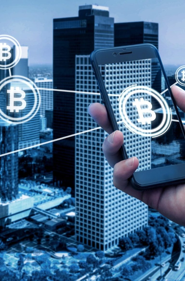 Hand in a smartphone, displaying Bitcoin symbols and buildings in the background.