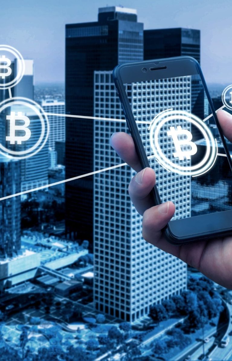 Hand in a city, holding a smartphone with Bitcoin symbols on the screen.